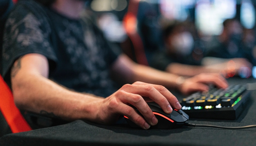 Male hands holding a black gaming mouse next to a mechanical keyboard during a competitive match.